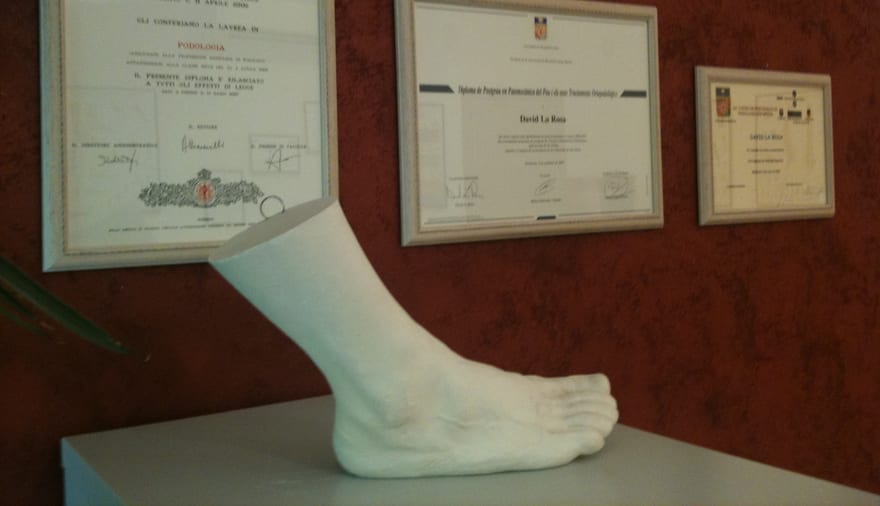 Tre diplomi incorniciati alla parete e, in primo piano, un calco in gesso di un piede